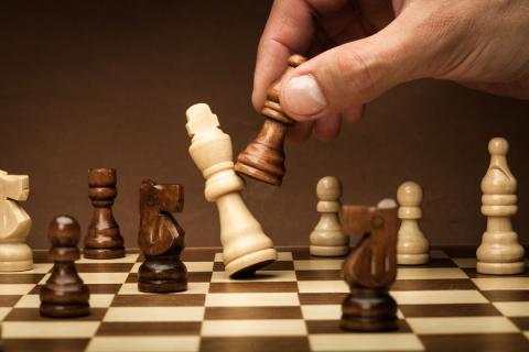 Chess board with a hand knocking a piece over with another piece.